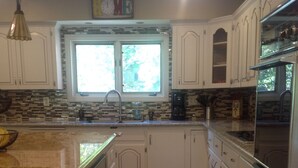 Una cocina con armarios blancos, encimera de granito, pileta doble y horno integrado.