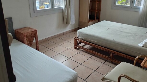 Quarto pequeno e limpo com duas camas, uma cadeira de madeira, uma mesinha e um guarda-roupa.