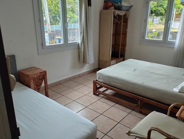 Une petite pièce propre, avec deux lits, une chaise en bois, une petite table et une armoire.