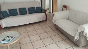 Uma sala de estar com dois sofás, uma mesinha e uma porta que dá para outro quarto.