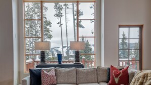 A cozy living room with a large window overlooking a snowy mountain landscape. - Harvest Moon Haven | Premier Ski Access + Hot Tub (Big Sky)