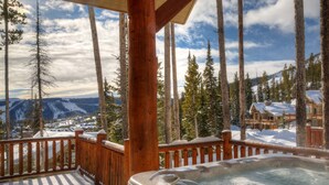 A wooden deck with a hot tub, overlooking a snowy mountain landscape and a lodge. - Harvest Moon Haven | Premier Ski Access + Hot Tub (Big Sky)