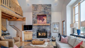 A spacious living room with a stone fireplace, a large window, and a cozy seating area. - Harvest Moon Haven | Premier Ski Access + Hot Tub (Big Sky)