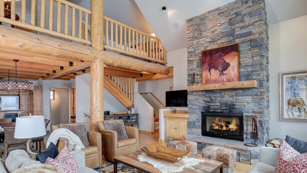 A spacious living area with a stone fireplace, leather furniture, and a wooden staircase. - Harvest Moon Haven | Premier Ski Access + Hot Tub (Big Sky)