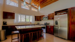 Una cucina moderna con mobili in legno, un frigorifero in acciaio inossidabile e una grande isola con sgabelli da bar.