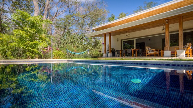 Una piscina cristallina con un’amaca, un pontile di legno e un’area salotto all’aperto.