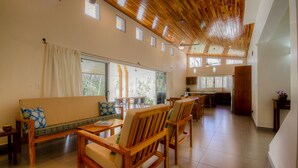 Un'ampia zona giorno con soffitto in legno, un divano, sedie da pranzo e una cucina sullo sfondo.