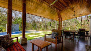 Una veranda esterna coperta con mobili in legno, un barbecue e una piscina.
