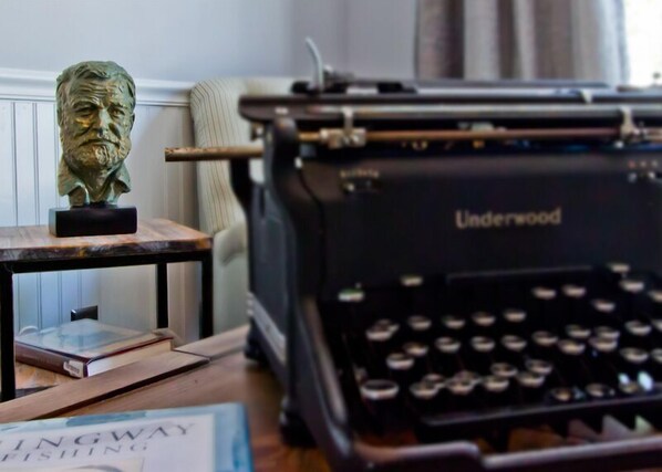 Une machine à écrire Underwood ancienne, un buste sculpté et un livre intitulé « TINGWAY FISHING » sont posés sur une table en bois.