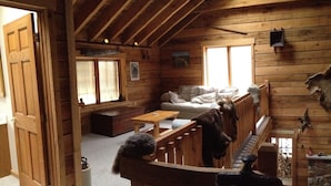 En mysig stuga med träpanel på väggarna, en soffa, ett soffbord och en hundkoja.