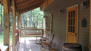 En veranda av trä med gungstolar och ett fat, med utsikt över ett skogsområde.