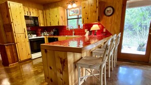 Une cuisine avec des meubles en bois, un crédence en carreaux rouges, une cuisinière en acier inoxydable et un coin bar avec des chaises blanches.
