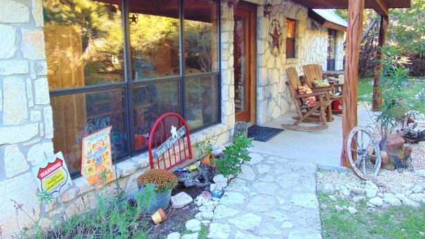 Un bâtiment en pierre doté de grandes fenêtres, d’un porche avec des chaises et d’un petit jardin.