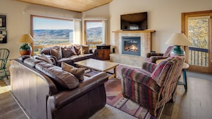 Ein gemütliches Wohnzimmer mit Ledersofas, einem Kamin und großen Fenstern mit Blick auf die Berge.