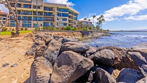A beachfront hotel with multiple balconies, a rocky shoreline, and palm trees. - Great Listing/Price/AC in the bedroom! (Maalaea)