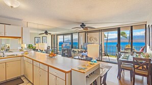 A modern kitchen with a large island, a dining area with a view of the ocean, and a balcony with a table and chairs. - Great Listing/Price/AC in the bedroom! (Maalaea)