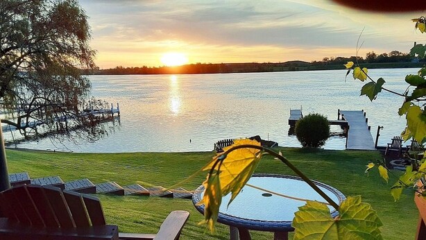 A deck with chairs and a table overlooking a lake at sunset.