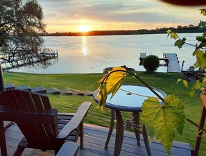 Une terrasse avec des chaises et une table, donnant sur un lac au coucher du soleil.