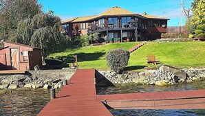 A house with a red dock leading to a water body, surrounded by greenery and a stone wall.