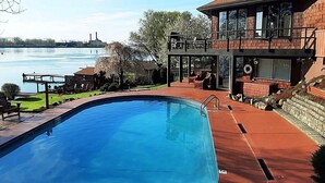 A swimming pool with a view of a river and a building with a deck and outdoor seating.