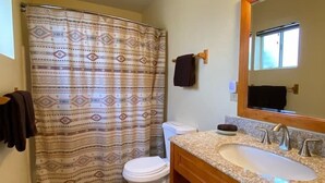 A bathroom with a patterned shower curtain, a white toilet, a sink with a mirror, and wooden cabinets. - Historic A-Frame Panoramic Red Rock Views! (Sedona)