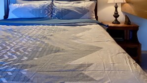 A bedroom with a wooden ceiling, a bed with patterned bedding, a nightstand with a lamp, and a painting on the wall. - Historic A-Frame Panoramic Red Rock Views! (Sedona)