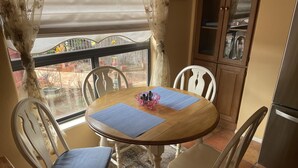 Een eethoek met een ronde houten tafel, vier witte stoelen en blauwe placemats.