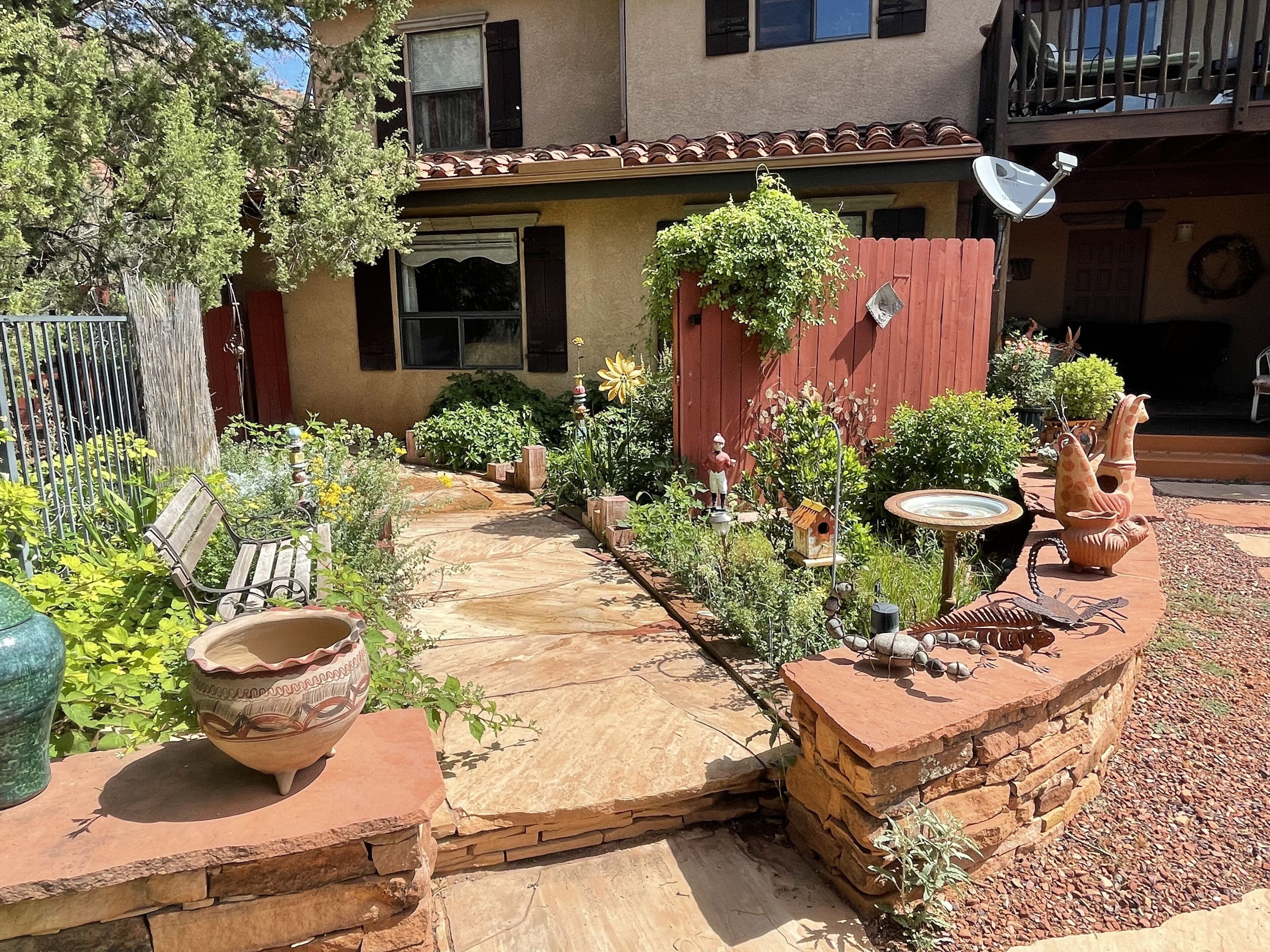 A courtyard with a stone pathway, a wooden bench, a birdhouse, and a decorative bird sculpture.