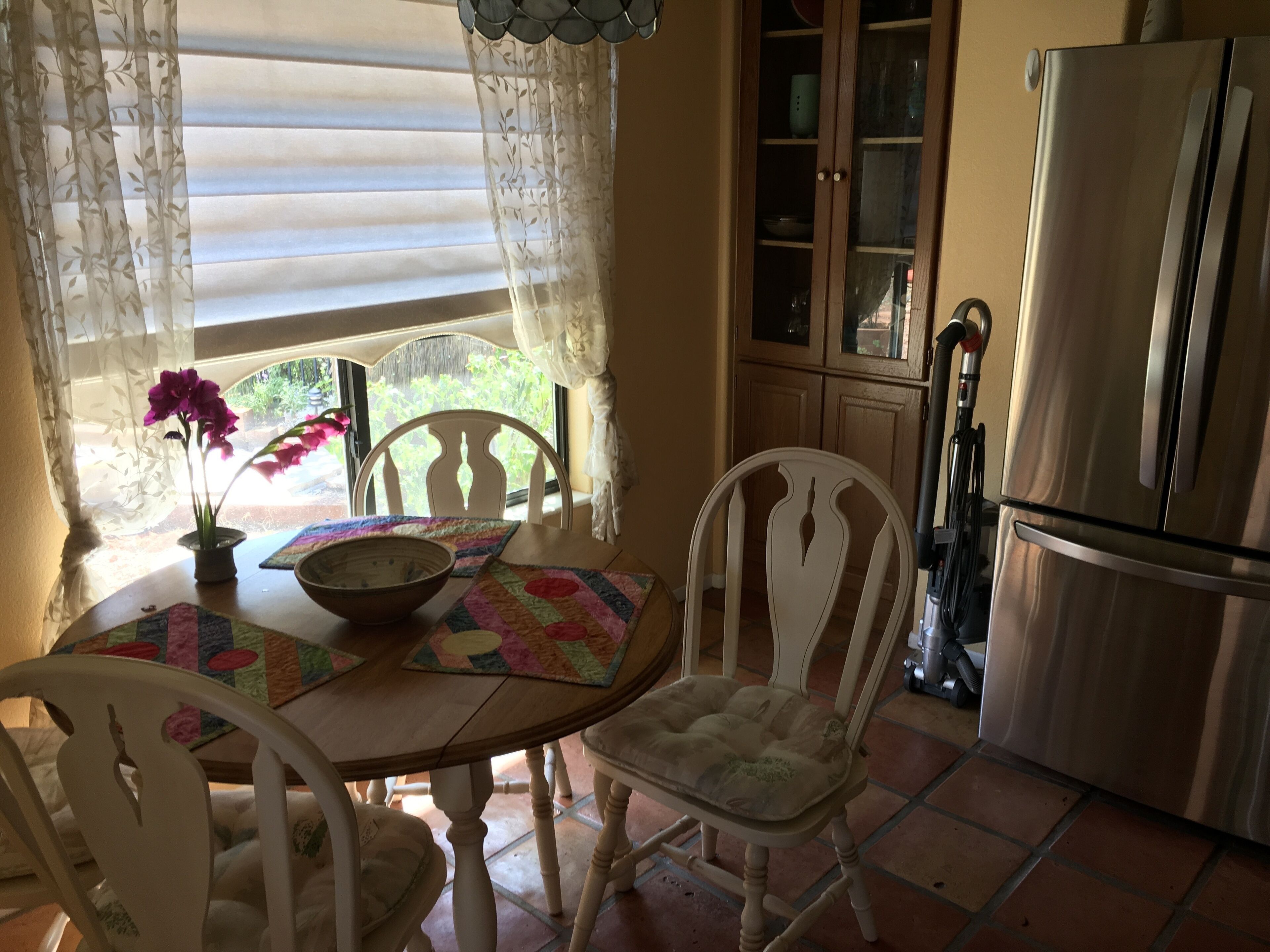 Een keuken met een eettafel, stoelen, een koelkast en een raam met gordijnen.