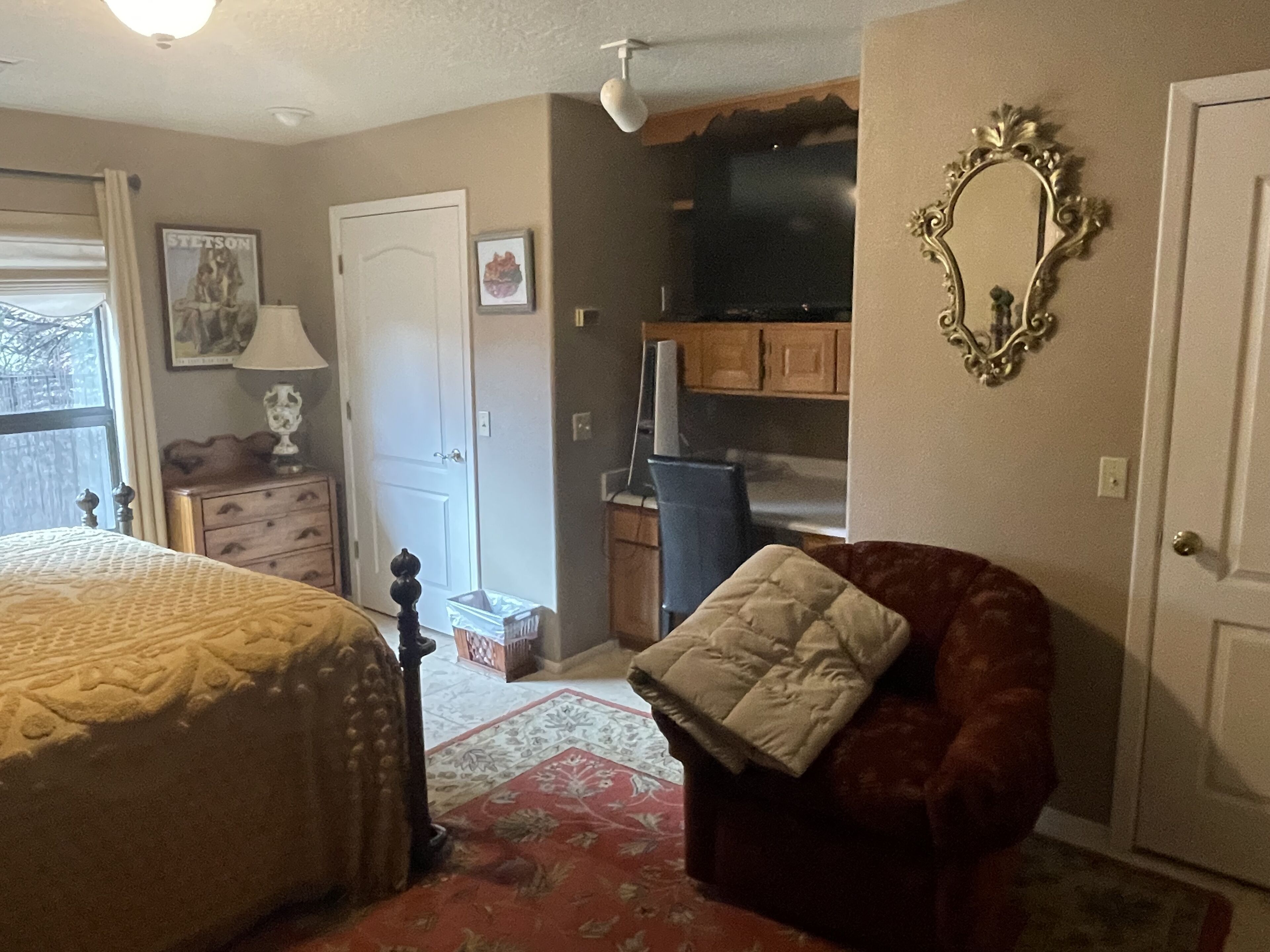 A bedroom with a bed, a chair, a dresser, a mirror, and a door.