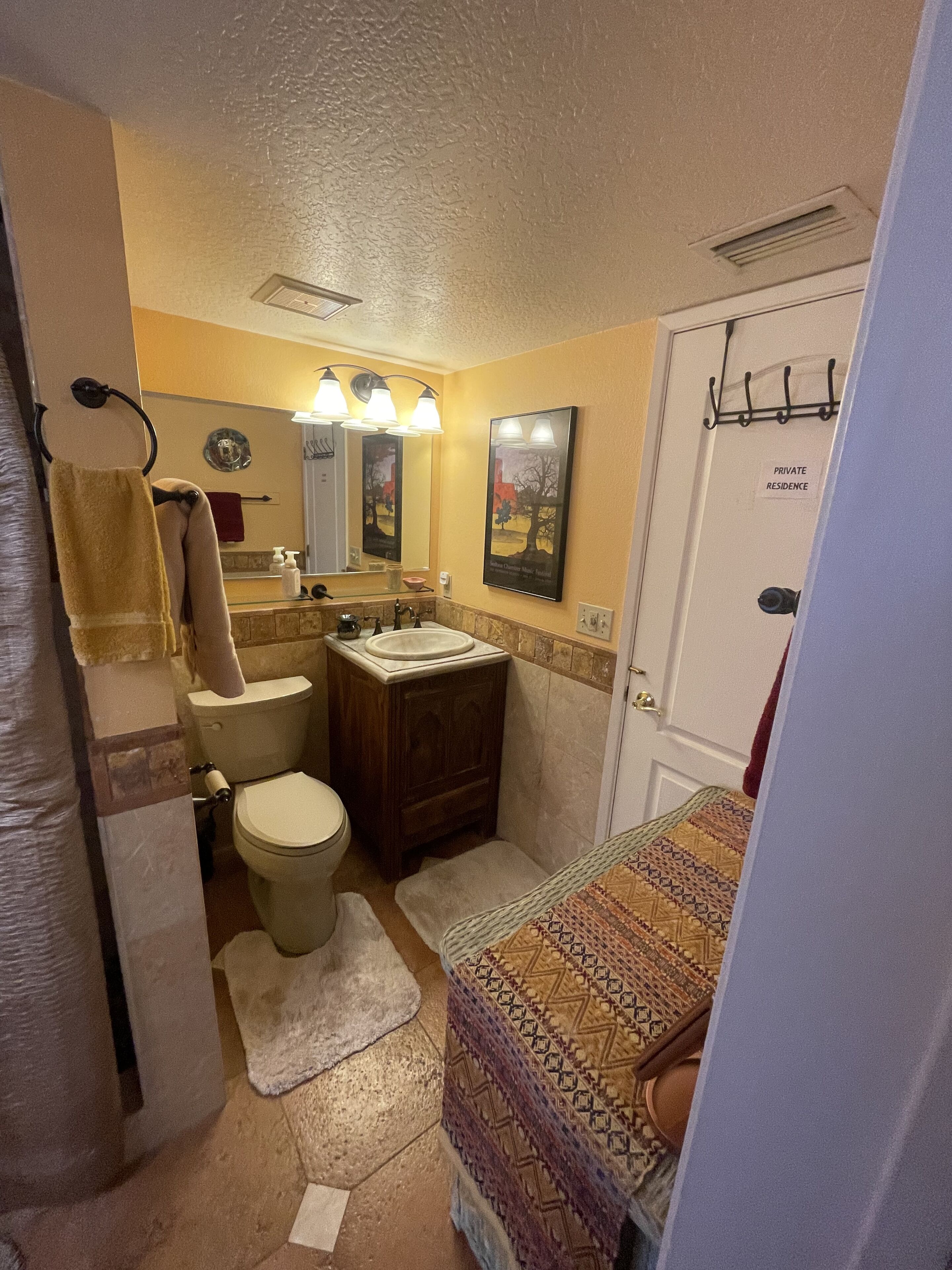 Une salle de bain avec des toilettes, un lavabo et un miroir. On y trouve un porte-serviettes et une porte sur laquelle est apposée une pancarte indiquant « RÉSIDENCE PRIVÉE ».
