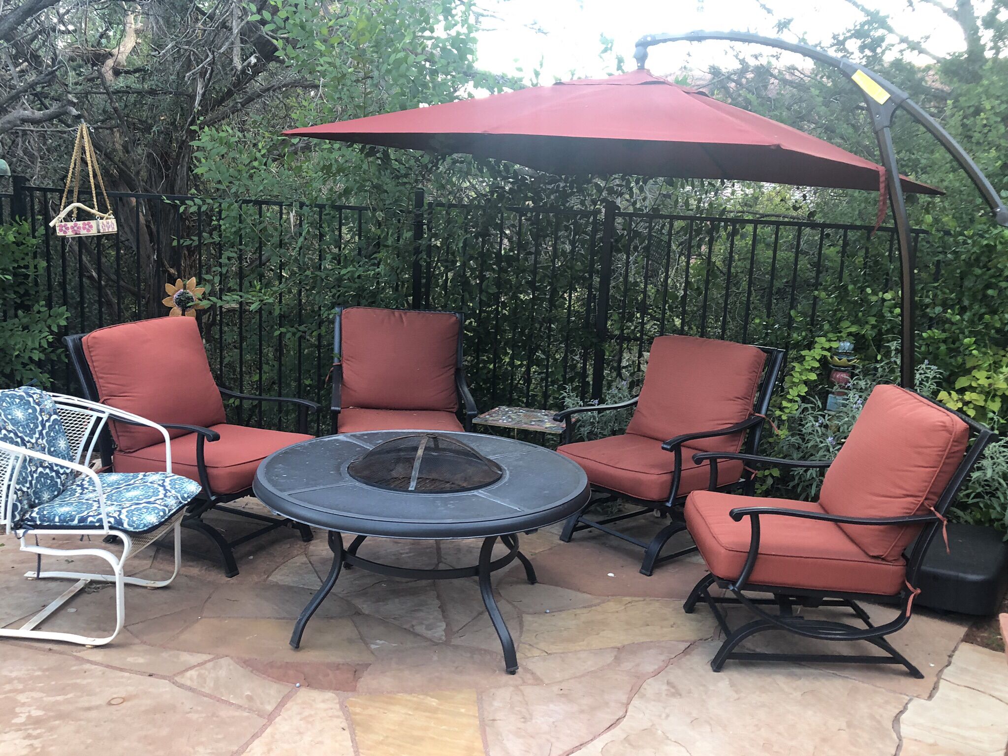 Eine Terrasse im Freien mit vier roten Sitzgelegenheiten, einem runden Tisch und einem Feuerkorb, sowie einem roten Sonnenschirm.