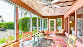 Una habitación iluminada por el sol, con una mesa de vidrio, sillas de madera y un ventilador de techo.