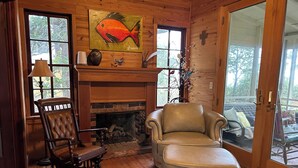 A cozy room with a fireplace, wooden flooring, a leather armchair, and a wooden rocking chair. - Bayfront Cottage. Private pier! Sunsets! Sunrises! 4 acres! New bike trail. (Gulf shores)