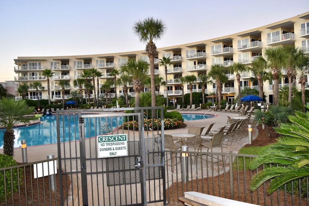 A hotel with a pool area, a gated entrance, and multiple balconies.