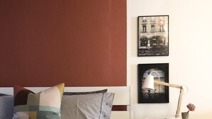A neatly made bed with striped bedding, a wooden nightstand with a lamp and a small vase, and two framed pictures on the wall.