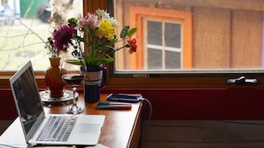 Una laptop sobre un escritorio con un florero de flores, una copa de vino y un teléfono inteligente.