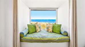 A room with a window overlooking a beach, a bed with striped bedding, and two pillows. - 1856 - The Coastal Canvas: Serene Beachfront (Fernandina Beach)