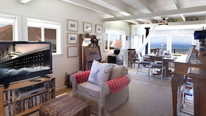 A cozy living room with a television, bookshelves, a sofa, and a dining area with a view.