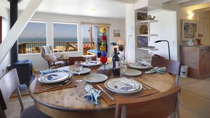 A dining area with a view of the ocean, a fireplace, and a dining table set with plates and glasses.