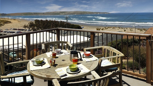 A wooden deck with a table set for dining, overlooking a beach and ocean.