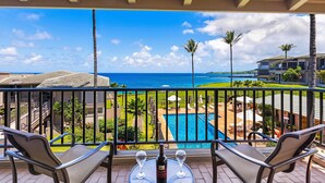A balcony with two chairs and a table, overlooking a swimming pool and a view of the ocean.