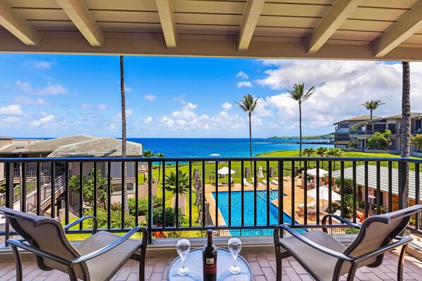 Un balcon avec deux chaises et une table, donnant sur une piscine et offrant une vue sur l’océan.