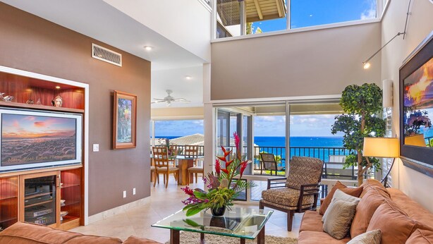 A spacious living area with a large flat-screen TV, comfortable seating, a glass coffee table, and a balcony with a view of the ocean.