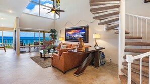 A spacious living area with a large window overlooking the sea, a comfortable sofa, a coffee table, and a modern staircase.