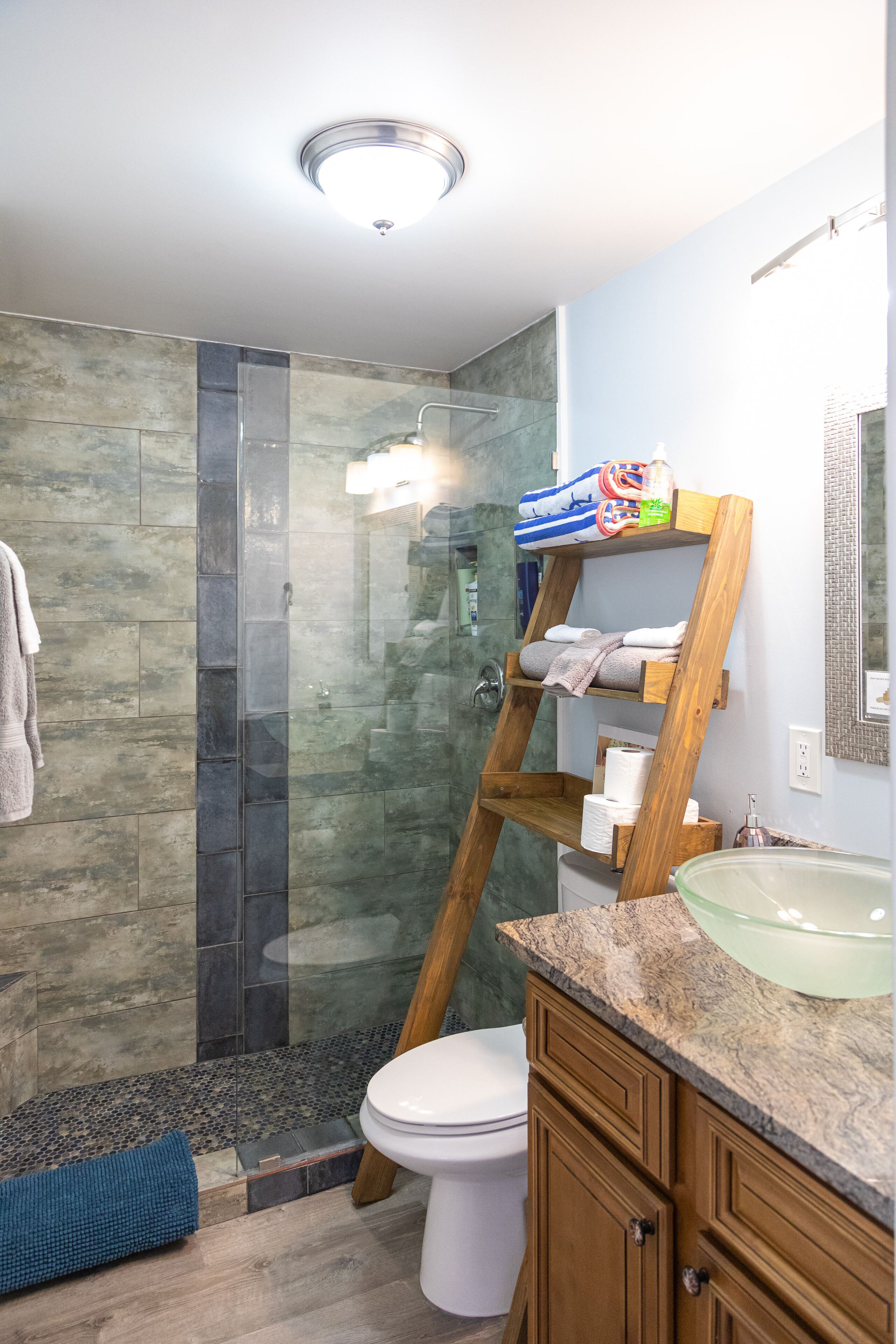 Un bagno moderno con cabina doccia in vetro, porta asciugamani in legno e piano di lavoro in marmo.