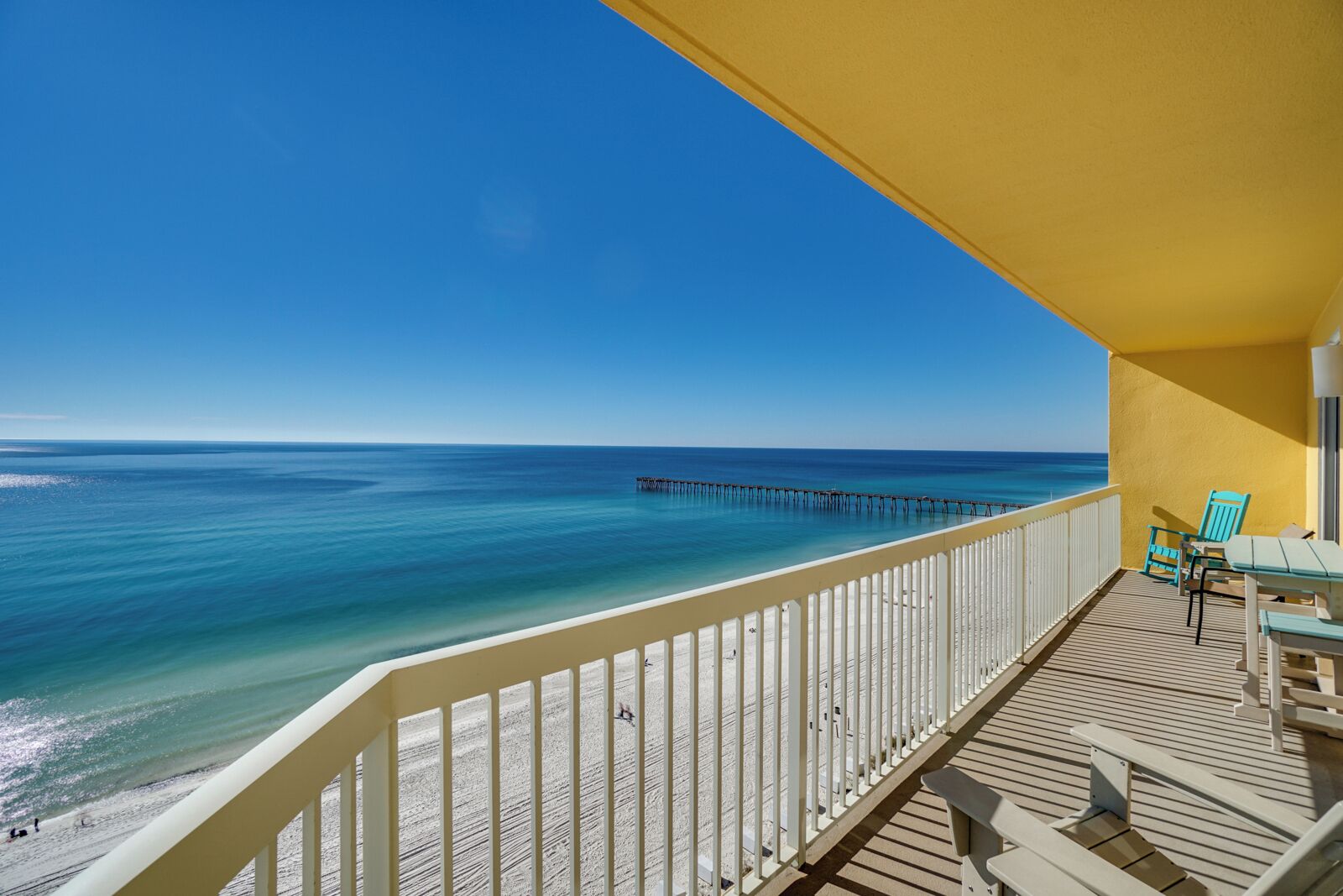 A balcony with a view of the ocean, a pier, and a yellow building.