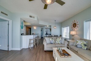 A spacious living room with a large sofa, a coffee table, and a kitchen area in the background.
