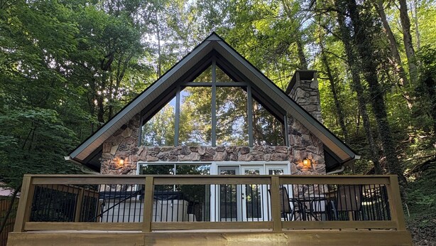 Eine Holzhütte mit Natursteinfassade, einer Holzterrasse und einem Schornstein.