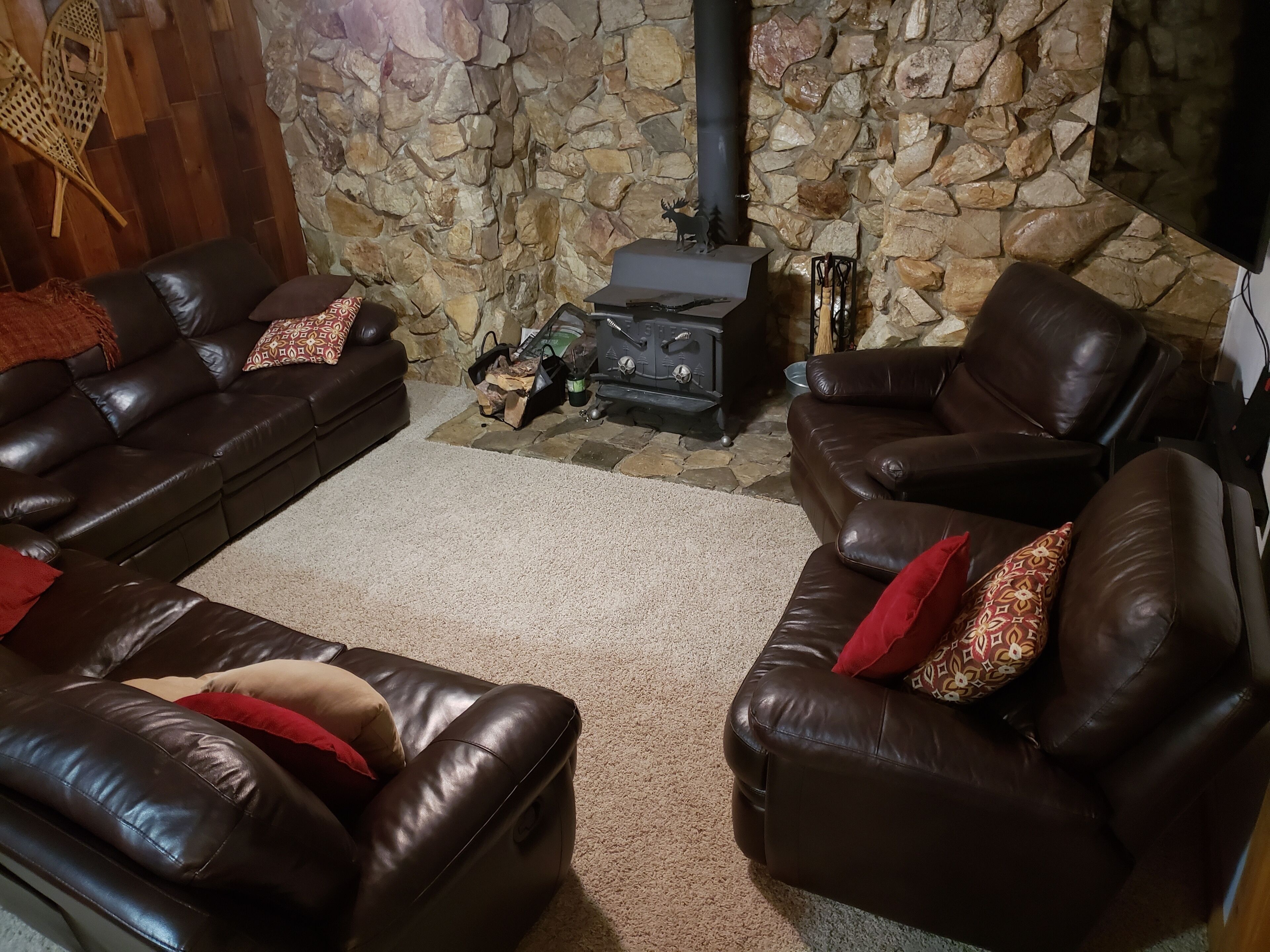 A cozy living room with two leather sofas, a stone wall, a fireplace, and a television.